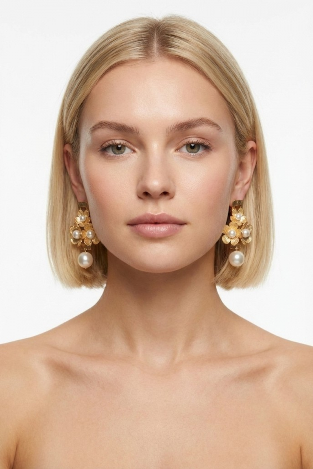 Boucles d’oreilles Versailles dorées ornées de fleurs ciselées et de perles fantaisie écrues, portées par une femme blonde au carré sur fond blanc. Bijou majestueux et raffiné.
