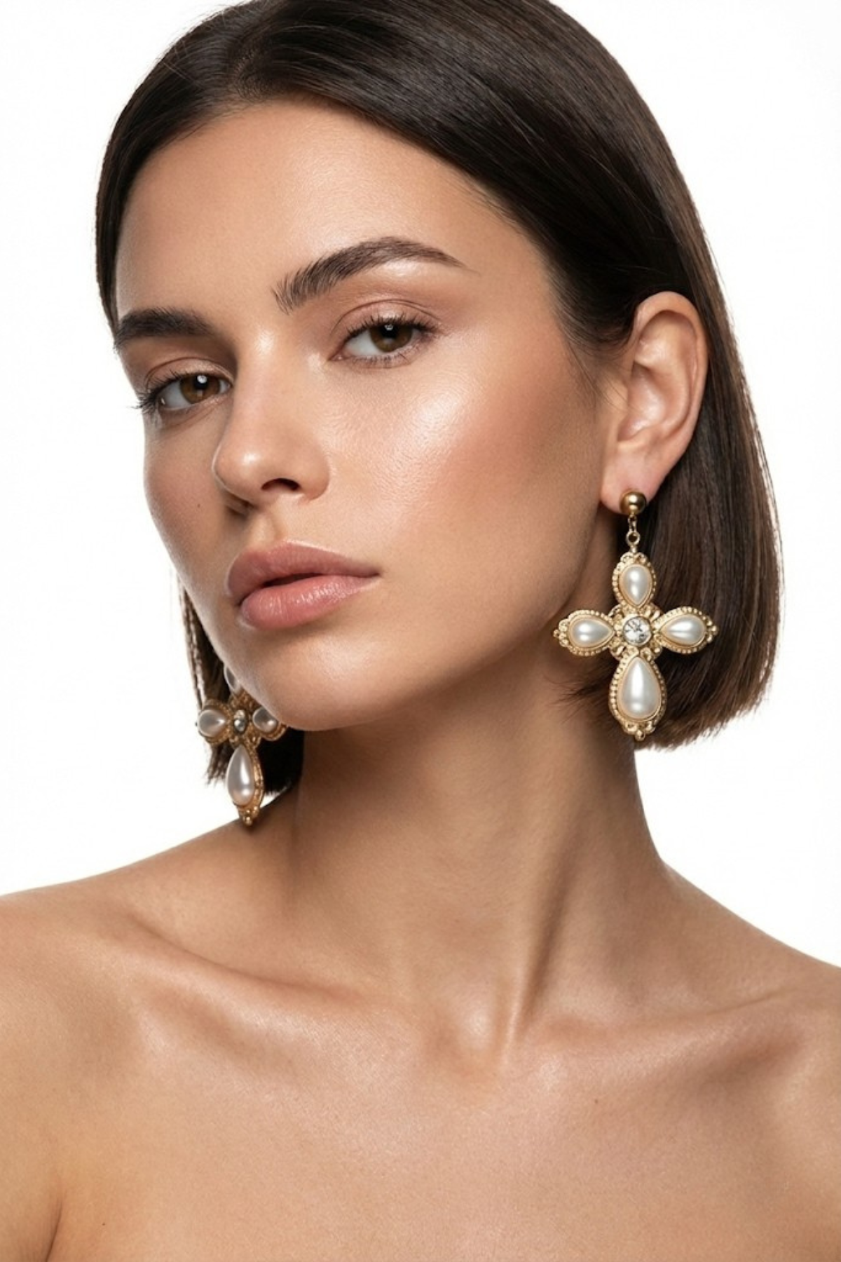 Boucles d’oreilles Élysée dorées en forme de croix, ornées de perles fantaisie écrues et de détails scintillants, portées par une femme brune au carré sur fond blanc. Bijou de mariage élégant et raffiné.