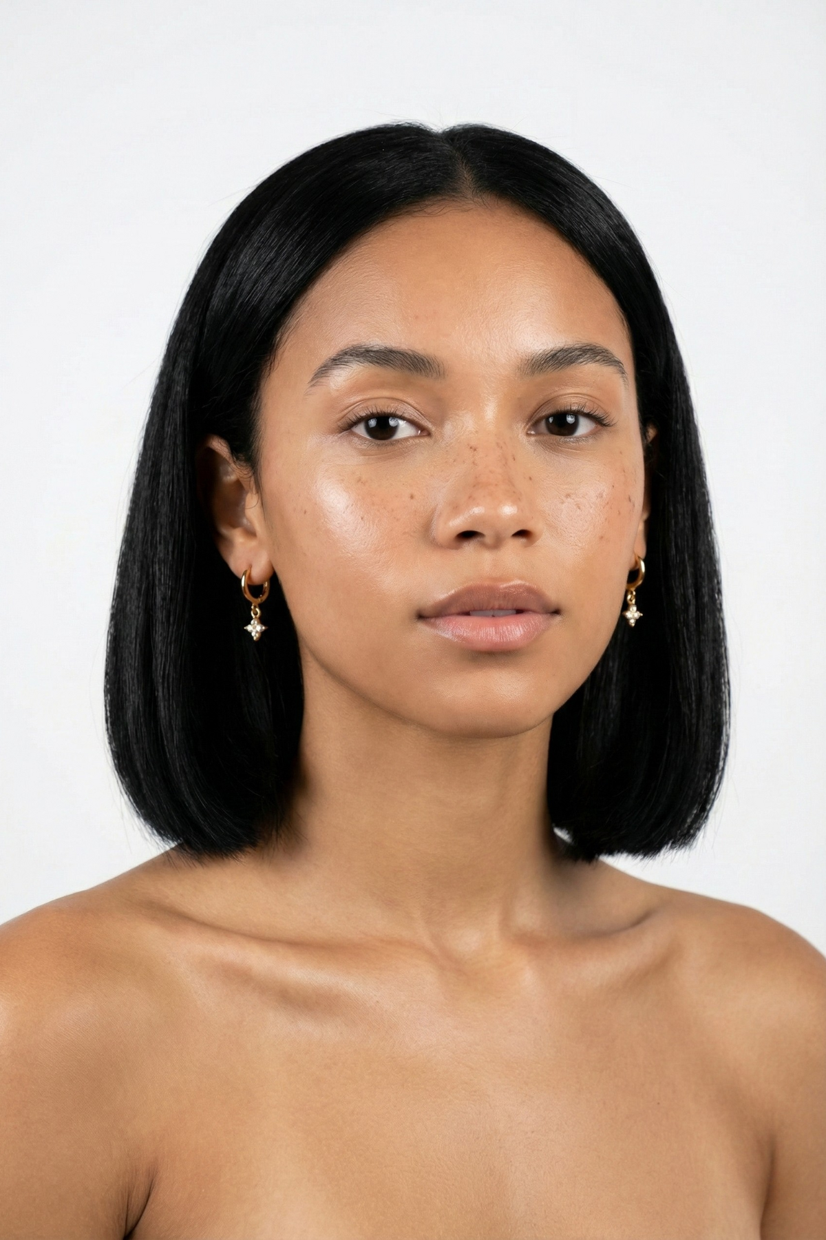 Boucles d’oreilles Opéra dorées avec pendentif trèfle à quatre feuilles serti de strass scintillants, portées par une femme brune au carré sur fond blanc. Bijou délicat et lumineux.