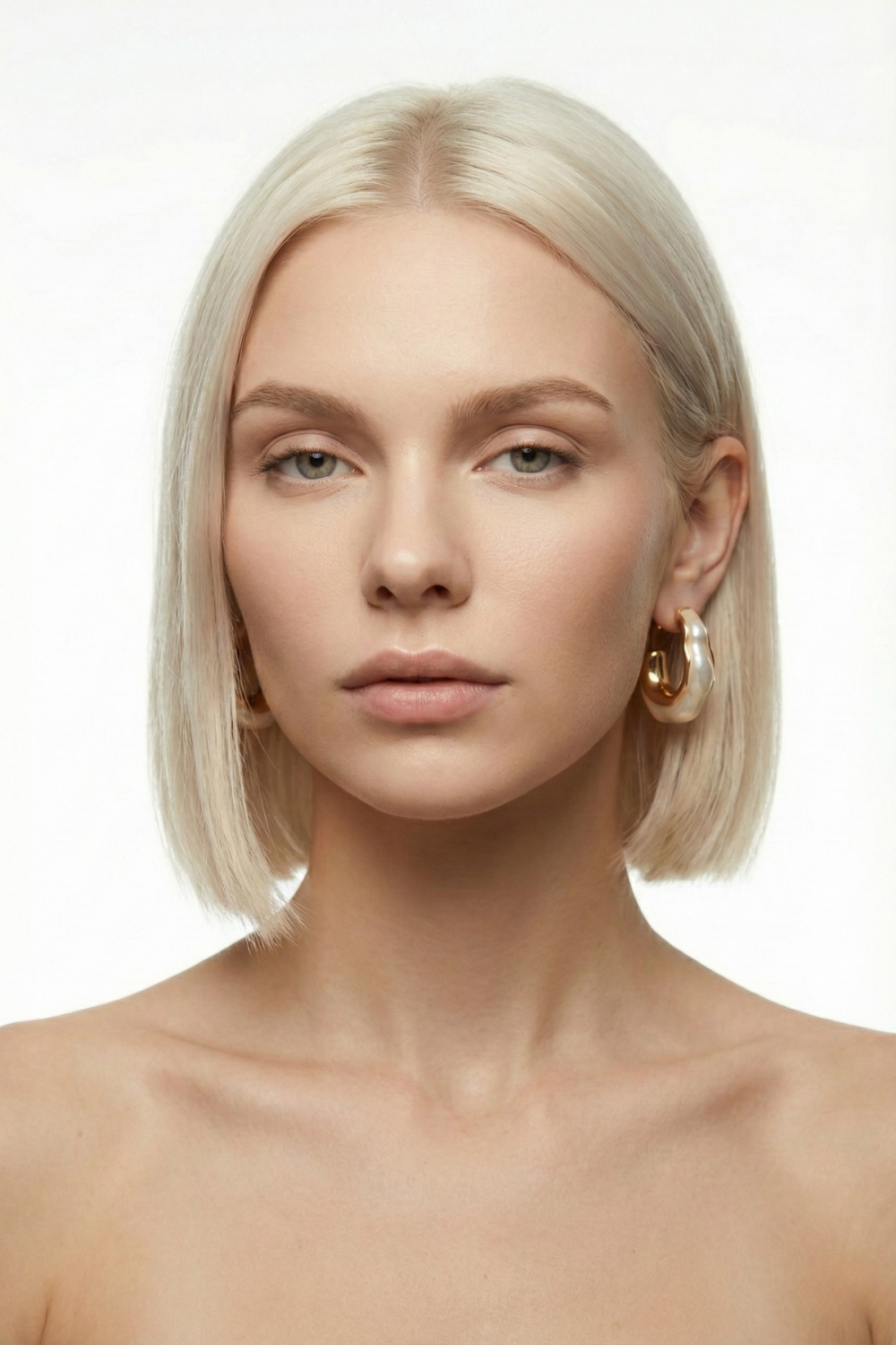 Boucles d’oreilles Palais-Royal dorées, au design ondulé asymétrique de 4 cm, portées par une femme blonde au carré sur fond blanc. Bijou sculptural, moderne et élégant.