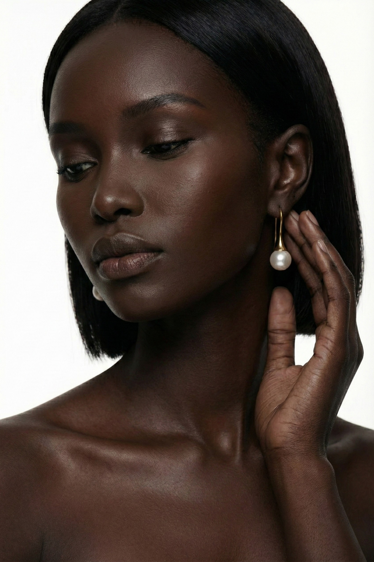 Boucles d’oreilles Rivoli dorées avec tige courbée et perle ronde blanche nacrée, portées par une femme brune au carré sur fond blanc. Bijou élégant, minimaliste et chic pour mariée.