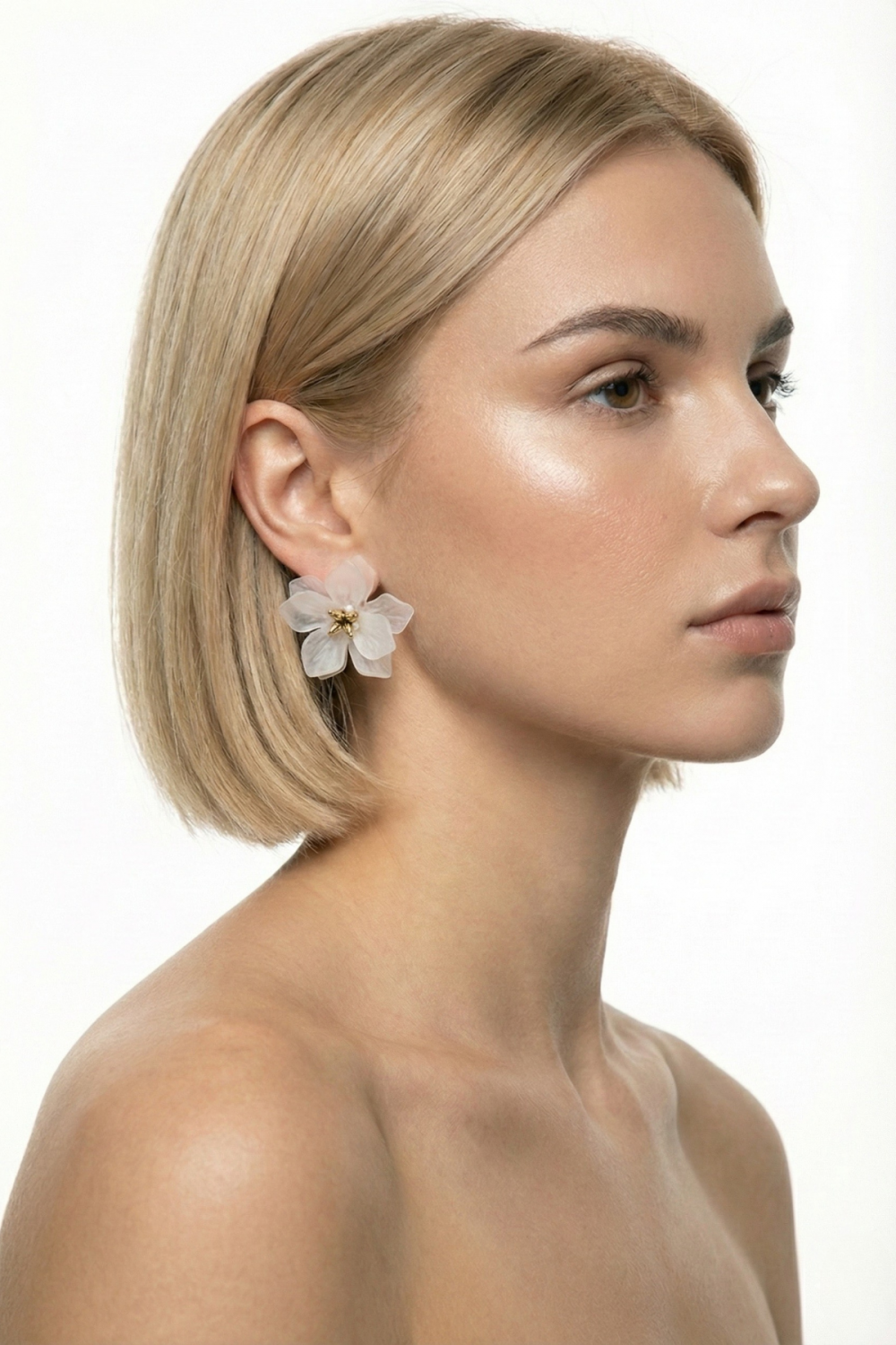 Boucles d’oreilles Tuileries en forme de grande fleur blanche cassée, montées en matière fantaisie, portées par une femme blonde au carré sur fond blanc. Bijou sculptural, léger et raffiné.