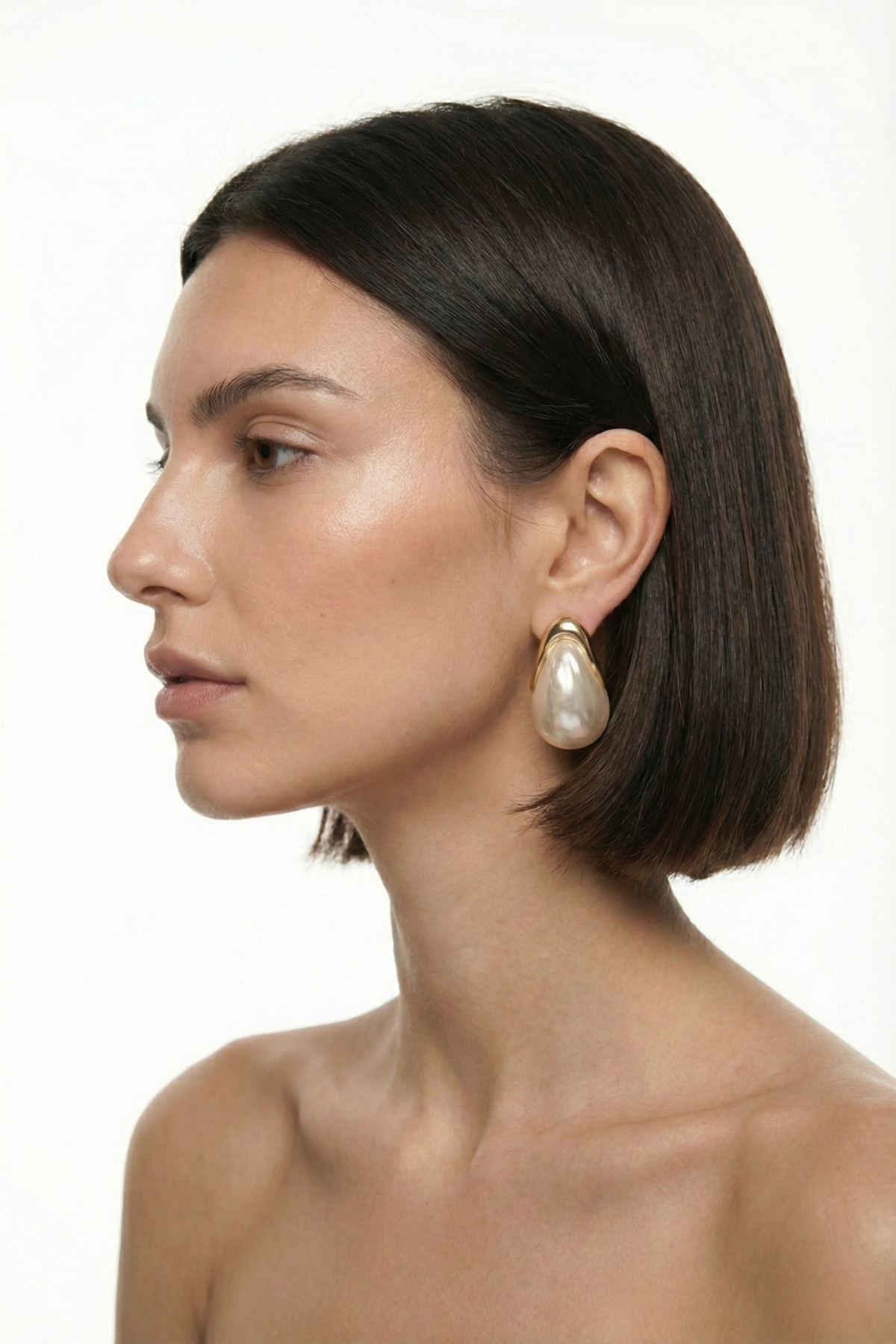 Boucles d’oreilles Vendôme dorées avec grande perle fantaisie écrue en forme de goutte, portées par une femme brune au carré sur fond blanc. Bijou élégant, minimaliste et raffiné.