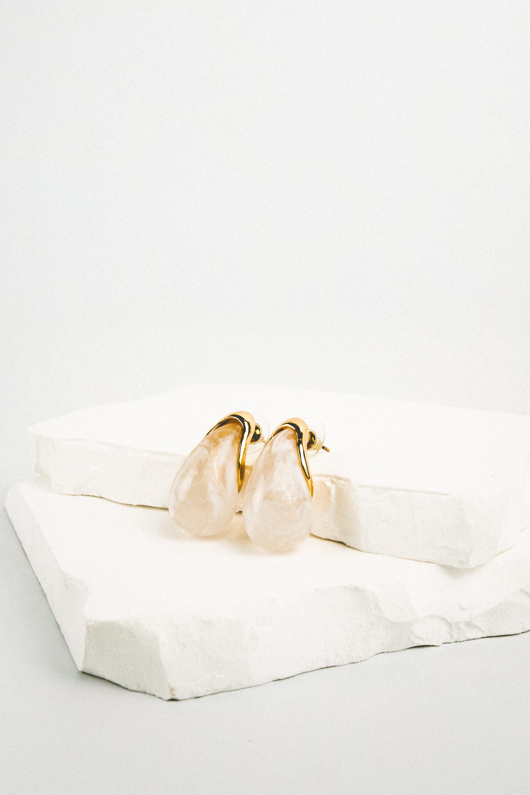 Boucles d’oreilles Vendôme dorées avec grande perle fantaisie écrue en forme de goutte, portées sur fond blanc. Bijou élégant, minimaliste et raffiné.