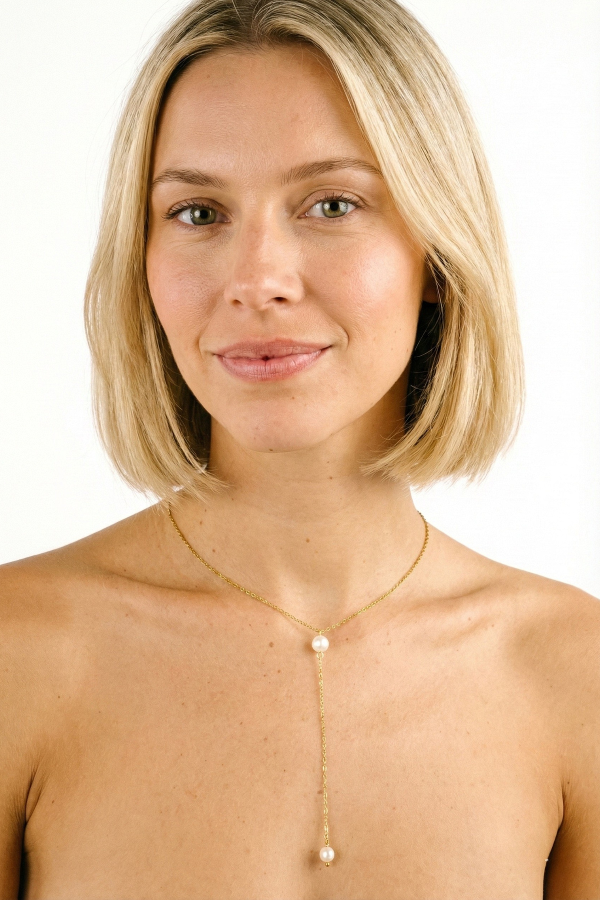 Collier Concorde doré en acier inoxydable, silhouette en Y ornée de deux perles blanches fantaisie, porté par une femme blonde au carré sur fond blanc. Bijou minimaliste et élégant.