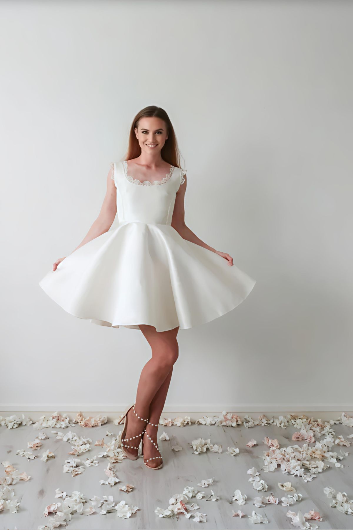 Mariée portant la robe Montmartre en soie et dentelle, coupe courte patineuse, posant dans un décor lumineux entourée de pétales, avec une allure chic et parisienne.