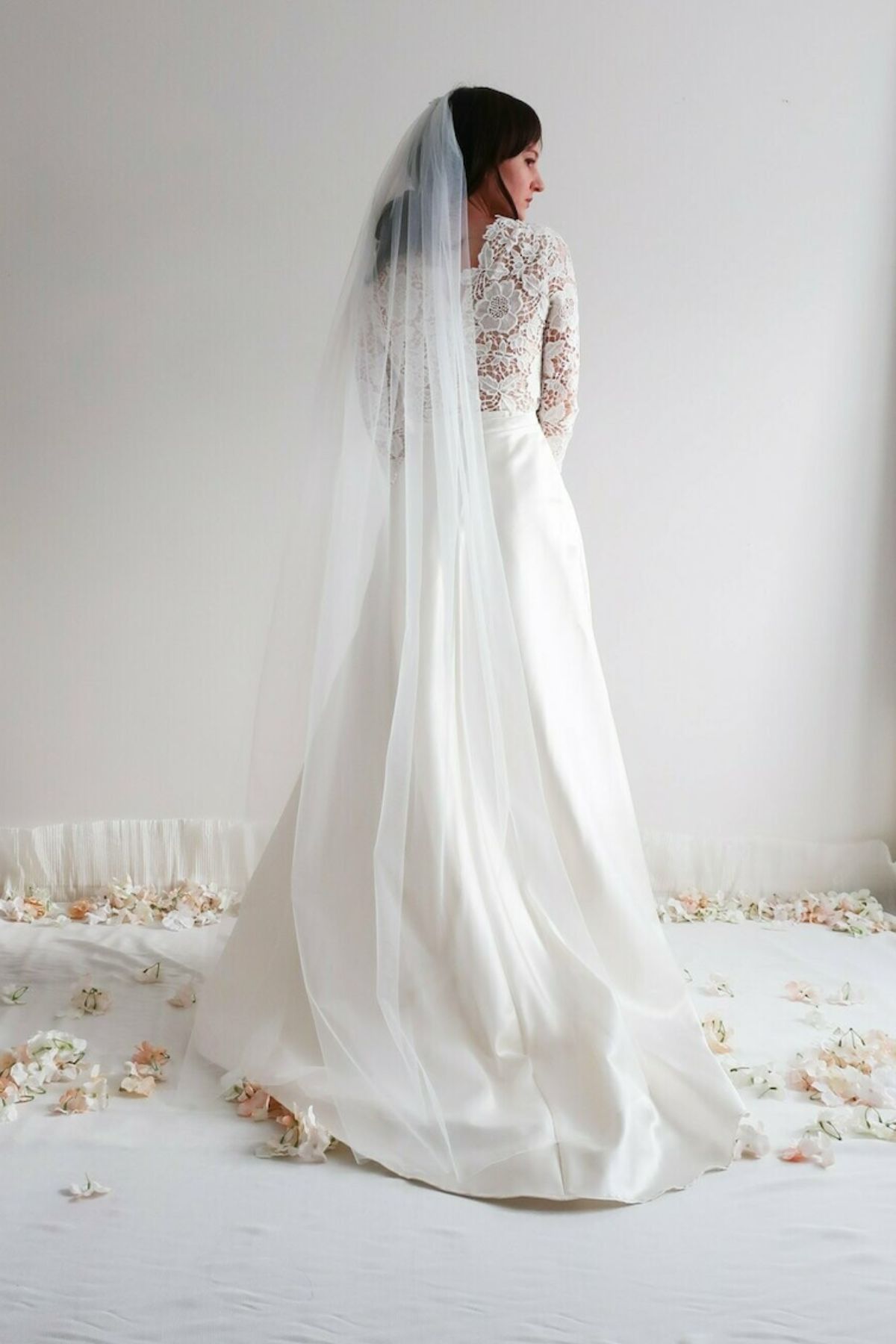 Mariée portant le voile Vanda long et fluide de 2 mètres, posé sur une robe en dentelle, dans un décor lumineux et romantique.